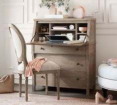 a desk with a chair and a vase on top of it next to a wall