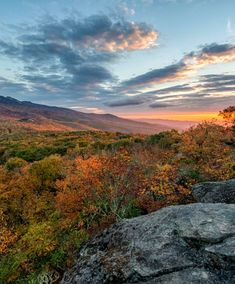 the sun is setting over some trees and hills in the distance, with rocks on either side