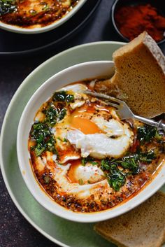 a bowl of soup with an egg in it on a plate next to some slices of bread