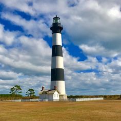 a large black and white lighthouse on top of a grass covered field