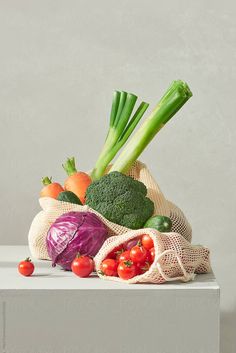 a bag full of vegetables sitting on top of a white counter next to tomatoes, broccoli and celery