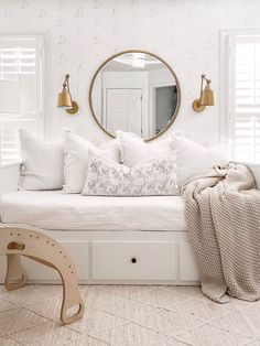 a white daybed with pillows and blankets on it in front of a round mirror