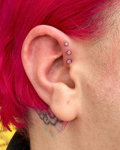 a woman with pink hair has two piercings on her ear and behind her ear