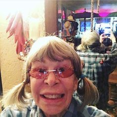 an older woman wearing glasses and smiling at the camera with other people in the background