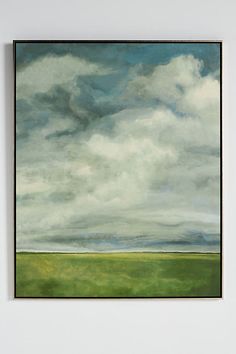 a painting hanging on the wall in front of a white wall with green grass and clouds