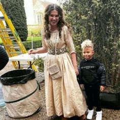 a woman in a dress standing next to a boy near a trash can and ladder