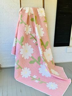 a pink and white flowered blanket sitting on top of a wooden chair next to a window