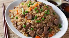 a white plate topped with beef and rice next to chopsticks on a table