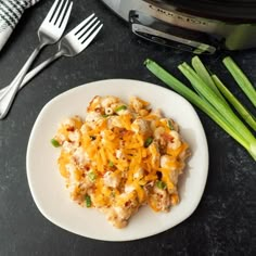 a white plate topped with macaroni and cheese next to green onions on a counter