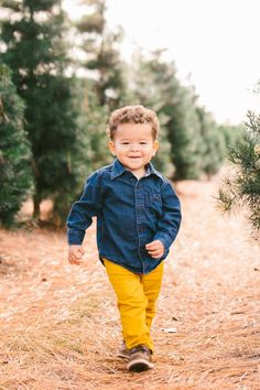 a little boy that is standing in the grass and smiling at the camera while wearing yellow pants