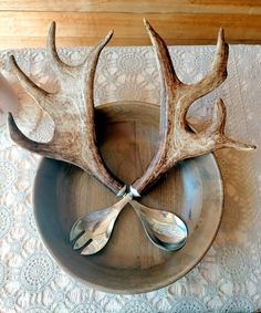 two antlers are sitting on top of a bowl with spoons in it,