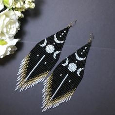 two pairs of black and white beaded earrings with crescents on them next to flowers