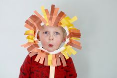 a young boy is wearing a paper lion mask with strips of orange and yellow tape around his face