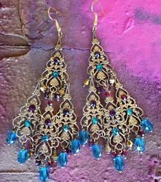 "These Antique Brass Filigree Moroccan Boho Chandelier Earrings are made with brass filigrees tiered to form a beautiful classic chandelier shape. Colorful crystal beads hang on each tier. Swarovski rhinestones add a touch of sparkle! Available with Posts, Clip-Ons, Leverbacks or French Wires. -4 1/2\" Long x 1 3/4\" Wide -0.4 oz. ea. Metal Finishes Available: -Antiqued Brass (as pictured) -Aged Bronze -Silver *As seen in the video Images show the 'Peacock Teal and Garnet', 'Ruby Red' & 'Bla Bohemian Jeweled Beaded Drop Earrings, Bohemian Jeweled Crystal Dangle Earrings, Festive Gold Jeweled Chandelier Earrings, Bohemian Blue Jeweled Earrings, Bollywood Jeweled Chandelier Earrings For Party, Festive Bohemian Jeweled Earrings, Gold Bollywood Beaded Earrings, Bollywood Beaded Gold Earrings, Bollywood Style Beaded Gold Earrings