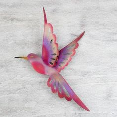 a pink and purple bird flying on top of a wooden table next to a white wall