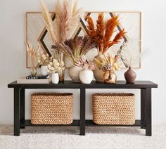 a table with two baskets and some plants on it next to a wall hanging in the background