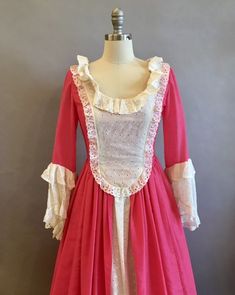 "Lovely reproduction colonial costume in deep, almost hot pink. The low square cut bodice is trimmed in white lace net. The bodice has an eyelet overlay. Three-quarter sleeves end in large draped net lace cuffs trimmed in more eyelet. The dress is fully lined in pink on the top and white eyelet that comprises the visible underskirt over which the pink upper skirt splits open in pannier style. The hem has a large ruffle over a stiff band that gives the skirt shape. Shown over a modest petticoat, Hamilton Costume, Colonial Costume, Pretty Gowns, Colonial Dress, Broadway Costumes, Navy Blue Cocktail Dress, Victorian Costume, Net Lace, Lace Cuffs