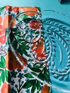 a glass plate and napkin on a blue table with oranges, leaves and flowers