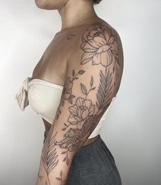 a woman with a flower tattoo on her arm and shoulder is standing in front of a white wall