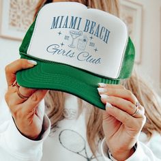 a woman holding up a hat with the words miami beach girls club written on it