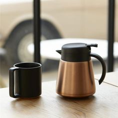 two black and copper coffee mugs sitting on a wooden table next to each other