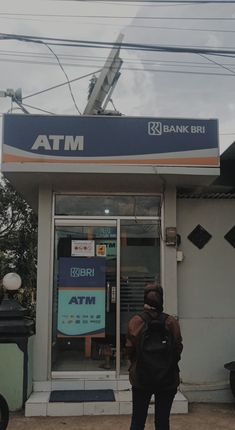 a person standing in front of a bank with a backpack on his back and an atm sign above the door