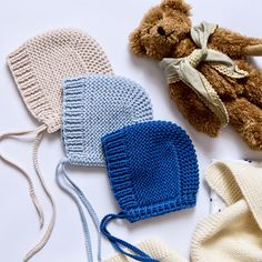 three knitted hats, one with a teddy bear on top and the other with a bonnet