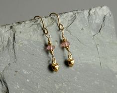 A sweet 14K gold heart charm swings below a peach pink tourmaline stone in these dainty small earrings. The peach pink tourmaline and charm hang from 14K gold filled ear wires. Darling and petite, these small feminine tourmaline earrings can be worn paired with a necklace, or alone, day or evening. A lovely gift or treat for yourself. These petite earrings measure just under 1 1/4 inches, including ear wires. Photos are taken close up, and may make stones appear larger. All variations, spots, an Dainty Pink 14k Gold Earrings, Pink Dainty 14k Gold Filled Earrings, Dainty Rose Gold Heart Dangle Earrings, Black Tourmaline Bracelet, Petite Earrings, Green Beaded Bracelets, Tourmaline Earrings, Tourmaline Bracelet, Tourmaline Jewelry