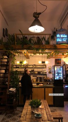 a man standing in front of a wooden table with plants on the shelves above it