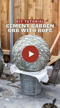 a metal ball sitting on top of a trash can next to a wooden fence with the words cement garden orb with rope