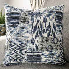 a blue and white pillow sitting on top of a gray couch next to a potted plant