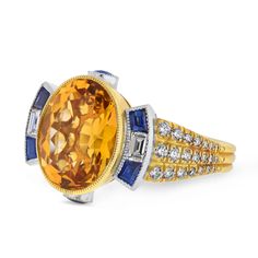 Discover timeless elegance with our handmade cocktail ring, a unique vintage-style Art Deco masterpiece crafted in our workshop. The centerpiece is a stunning 8.02cts citrine, bezel-set in a warm 18K yellow gold embrace. Accentuating its beauty, baguette blue sapphires and diamonds grace each side, creating an exquisite and one-of-a-kind design. The platinum and 18K yellow gold setting ensures durability and sophistication. Blue sapphires contribute 0.54 carats of vibrant allure, while round-cut diamonds, totaling 0.62 carats, add a touch of brilliance. This exceptional ring, sized at 7, weighs 14.00 grams, making it a perfect statement piece for any occasion. Elevate your style with this captivating blend of vintage charm and contemporary craftsmanship. Luxury Gold Sapphire Ring In Art Deco Style, Luxury Yellow Gold Baguette Cut Sapphire Ring, Luxury Gold Art Deco Sapphire Ring, Luxury Yellow Gold Sapphire Ring With Baguette Cut, Luxury Faceted Sapphire Ring In Yellow Gold, Luxury Yellow Gold Sapphire Ring With Gemstone Accents, Luxury Yellow Gold Elegant Sapphire Ring, Luxury Yellow Gold Sapphire Ring With Rectangular Shape, Luxury Antique Yellow Gold Sapphire Ring