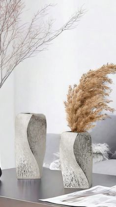 two vases sitting on top of a table next to a plant in a vase