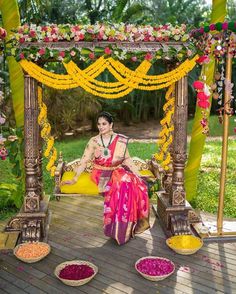 a woman sitting on top of a wooden floor under a yellow and pink arch covered in flowers