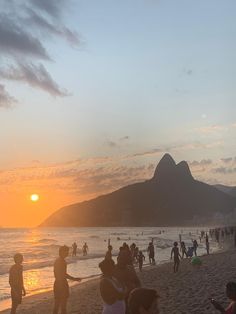 many people on the beach at sunset with mountains in the backgrouund and clouds in the sky