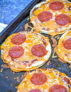 four pepperoni pizzas sitting on top of a baking sheet covered in cheese and sauce