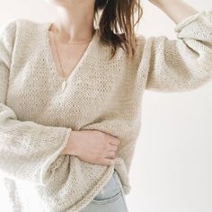 a woman wearing a sweater and holding her hand on her hip while standing in front of a white wall