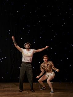 two people are dancing on a stage with stars in the background and one person is holding his arms out