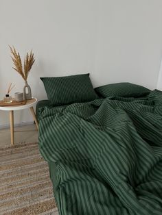 an unmade bed with green sheets and pillows on the floor next to a table