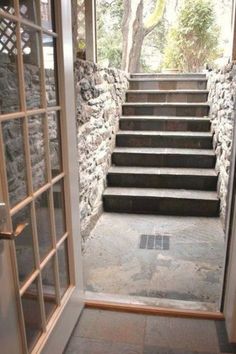 an open door leading to a set of stairs with stone walls and windows on either side