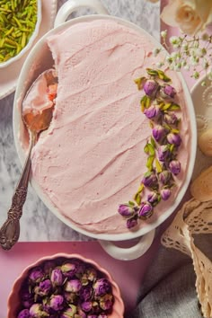 a cake with pink frosting and purple flowers on it next to bowls of dried flowers