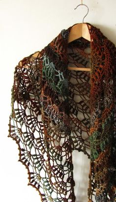 a crocheted shawl hanging on a wall next to a wooden hanger