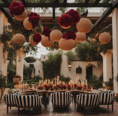 an outdoor dining area with black and white striped chairs, red flowers hanging from the ceiling