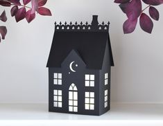 a black paper house sitting on top of a table next to a plant with purple leaves