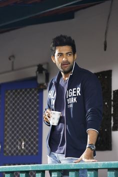 a man holding a coffee cup and looking at the camera while standing next to a railing