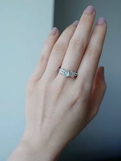 a woman's hand holding an engagement ring with two stones on it and the other side