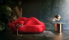 a red couch sitting on top of a wooden floor next to a table and lamp