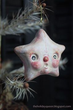 a ceramic star ornament hanging from a christmas tree with eyes and nose painted on it