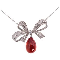 This is a refined necklace: a feminine bow with a sophisticated work reminiscing the Edwardian Belle-Epoque era, set with white diamonds, from which dandle a striking, pear-shaped cabochon tourmaline displaying a radiant pinkish-orange color. The make is excellent with openwork and millegrain setting. the diamond's quality is G VS, with the center one weighing ± 0,38 carat. Dimensions : 5,8 x 5 cm - Length 42,5 cm Tourmaline : 26,09 carat - Weight 21,4 grams Bow Pendant, Rose Orange, Color Rosa, White Diamonds, White Gold Diamonds, Diamond White, Orange Color, Tourmaline, Gold Diamond