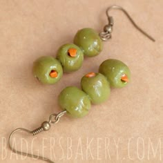 three green olives with orange centers are hanging from silver earwires on a brown surface